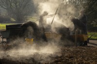 Steam rising from a pile of compost and gardeners shovelling it onto the ground at Kew Gardens, London.
