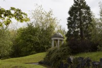 A domed classical temple on a grassy knoll. Trago Mills show gardens, Devon, UK. May. Spring