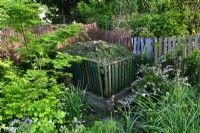 Wooden composter in the corner of the garden filled with fresh plants.