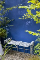 Repurposed upcycled modern contemporary metal bench seat made from an IBC - intermediate bulk container frame - on a gravel surface patio against a blue painted wall - Crataegus monogyna - Hawthorn and Corylus avellana - Hazel branches 