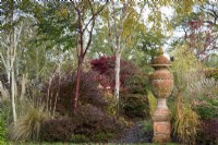 Terracotta urn surrounded by shrubs, ornamental grasses and trees including Prunus serrula and white-stemmed birches in November