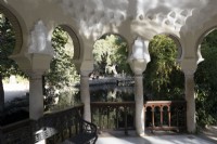 Looking out from inside a pergola on an island, accross a lake, with Islamic style arches. Parque de Maria Luisa, Seville, Spain. September