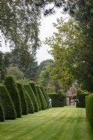 Yew topiary edges a lawn at The Manor, Little Compton with a view to a summerhouse.
