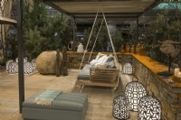 A sitting area on a gravel surface surrounded by a low stone fence with a wooden swing with pillows among many bright luminescent waterproof handmade decorative lamps in Luxurious African lodge.
Designer: Vetschpartner, Berger Gartenbau and Livingdreams. Giardina-Zurich, Swiss.






