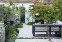 In this city garden, the outdoor kitchen and the sitting area, are paved with large sandstone paving stones, they are bordered with multi-stem Amelanchier canadensis, Veroniscatrum virginicum 'Fascination', Pittosporum tobira 'Nanum', Pinus mugo and Hakonechloa macra; a  Parrotia persica provides dappled shade and Thymus praecox 'Albiforus' runs in between the paving stones.