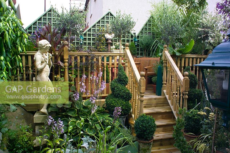 Small town garden in Bristol packed with plants in pots. Raised decking, steps and statue of Pan