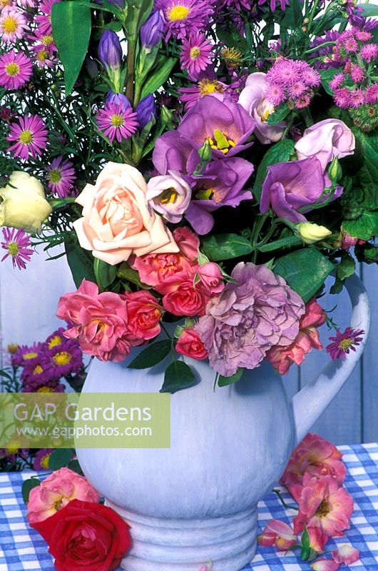 Late summer floral arrangement in blue jug - roses, hibiscus, asters, godetia and gentian