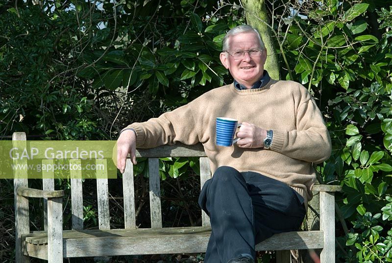 Mr Richard Ayres (retired Head Gardener from Anglesey Abbey, National Trust) sitting on wooden bench in Richard Ayres' Garden, Lode, Cambridgeshire
