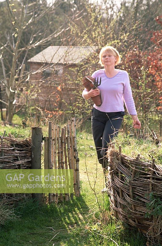 Woman walking through garden, clutching trowel and fork - Spring