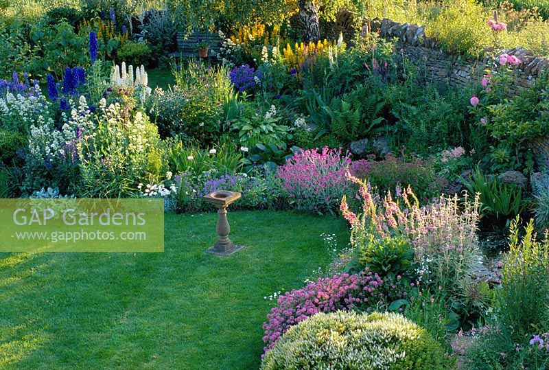 Border beside pond with lawn and sundial, planted with Hebe rakaiensis, Phuopsis stylosa, Verbascum and Lychnis flos-jovis - Oxfordshire