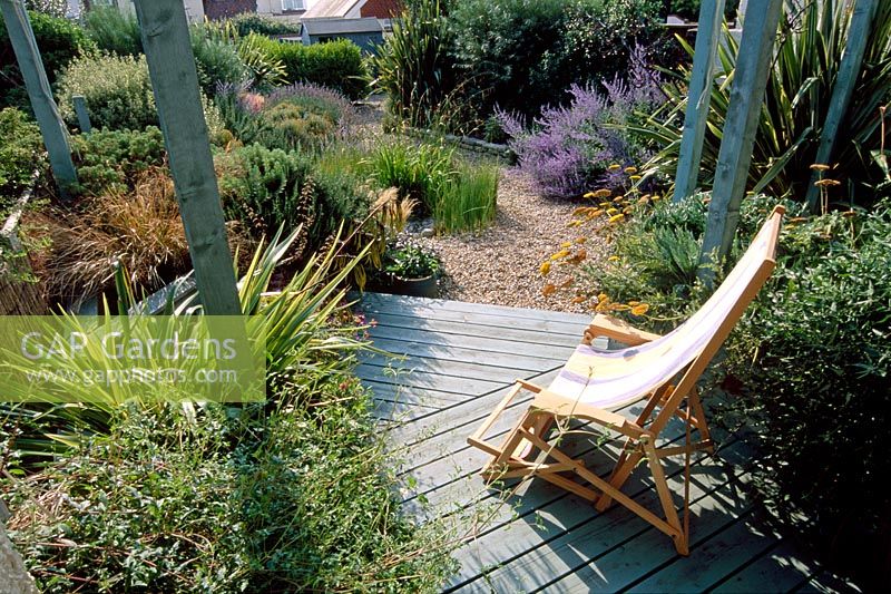 Seaside front garden with wooden verandah, pergola, deckchair, Phormiums and Perovskia