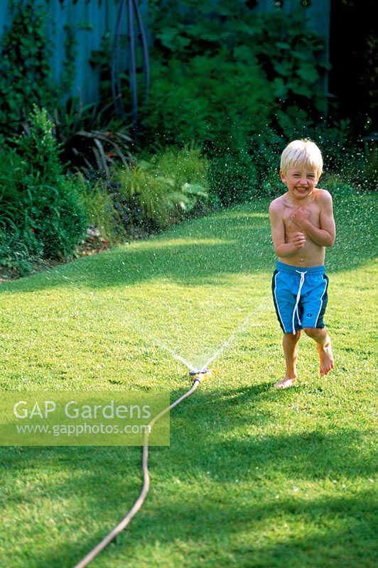 Young boy playing with a hosepipe in the garden