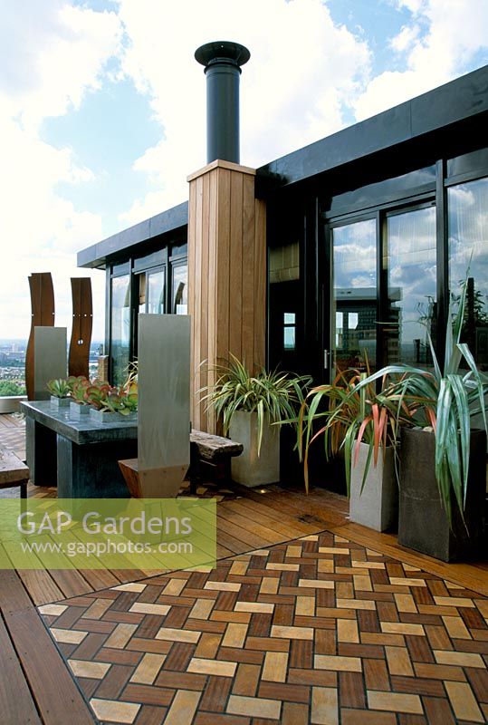 African themed roof terrace with iroko decking with inset herringbone design panels in coloured wood, zinc-wrapped table and stainless steel throne chairs