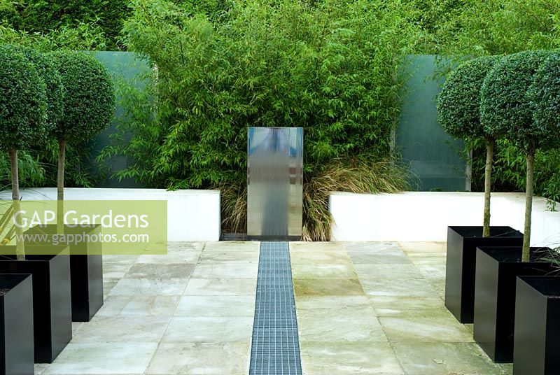 Small contemporary paved urban garden with stainless steel water feature and rill Designer Paul Dracott