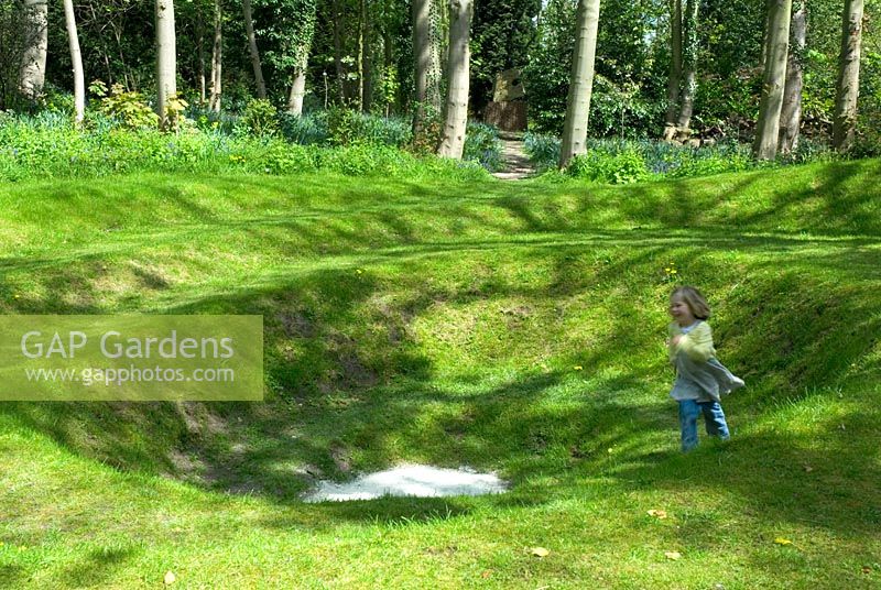 Child running around grass earth sculpture in spring woodland 