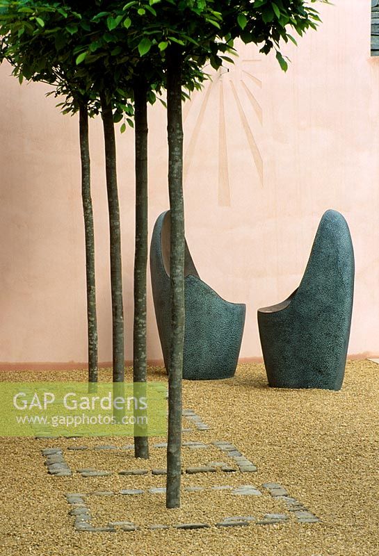 Two rounded metal seats in front of pink walls with sundial and row of clipped Carpinus trees in foreground - Lladro's Sensuality Garden, Chelsea 2003 