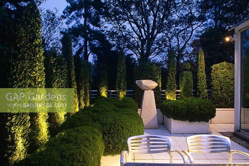 Roof garden with evergreen topiary and sculpture lit at night - London