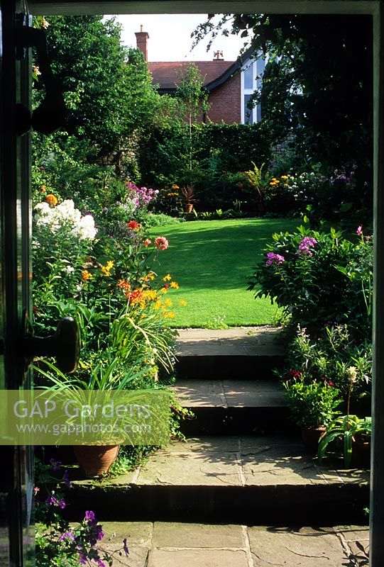 Traditional cottage style small urban back garden with Yorkstone paving steps. Plants include Crocosmia Dahlia and Phlox - Mews Cottage, Harrogate, Yorkshire