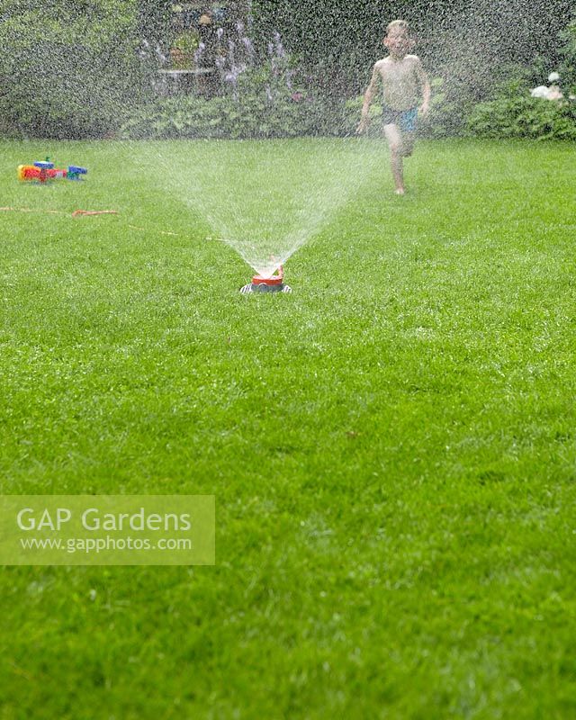 Boy running on grass with sprinkler 