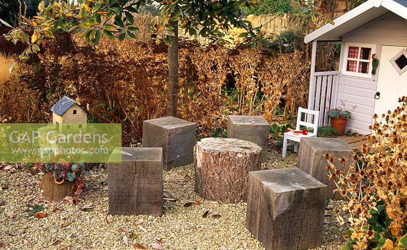 Wendy house surrounded by seedheads of Ergyngium giganteum and Ligusticum lucidum with pots of Echeveria elegans on the porch and cubes of wood as seats and tables - Yews Farm, Somerset