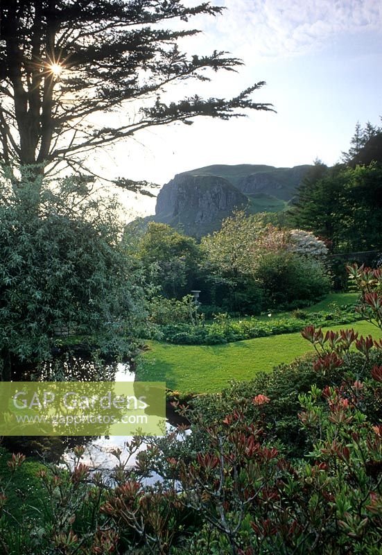 Stream beside lawn in garden with mountain in background - An Cala, Dumfries, Scotland

