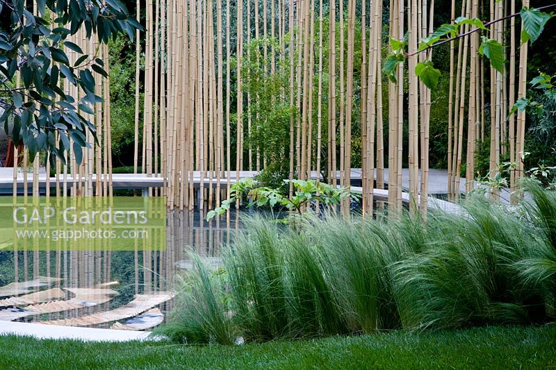 Pool with bamboo poles and raied walkway. Grasses in foreground. Garden in the Silver Moonlight, Design Haruko Seki and Makoto Saito. Sponsor - Royal Palm Residences Seychelles, Urban Regenerate Association of Niigata Supported by - The Great Britain Sasakawa Foundation, The Japan Society

