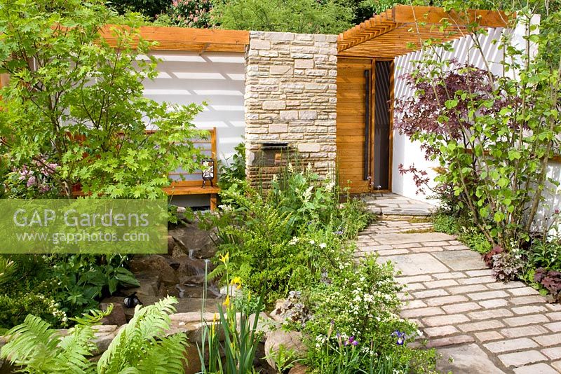 Sunny front garden with slatted roof over wooden bench and porch. Planting includes Acer palmatum cultivars, ferns, Irises and Corylus - Tokyo City Garden, Chelsea Flower show 2008
