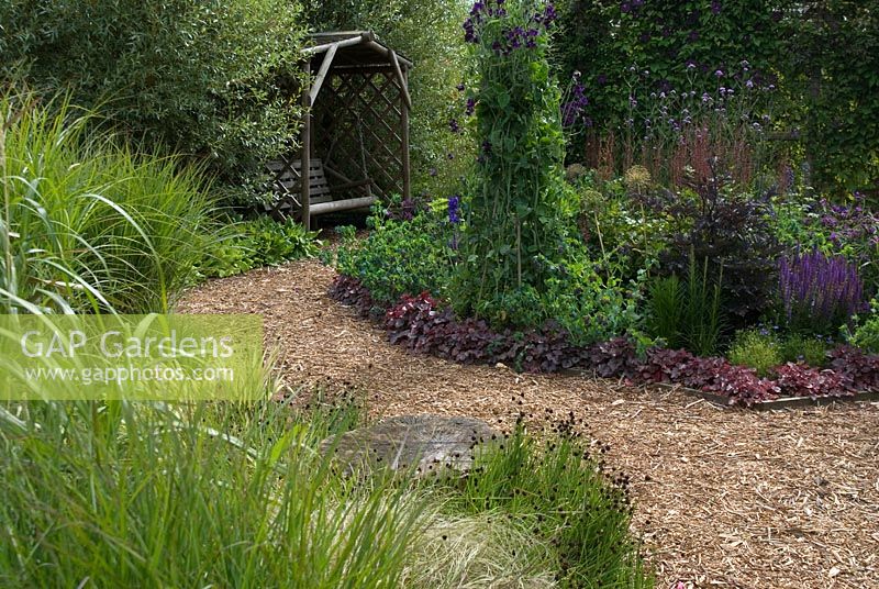 Herbaceous border and ornamental grass border with bark chippings path leading to a wooden arbour with swinging wooden seat - The Rainbow garden, 'Wedgwood', Hesketh Bank, Lancashire