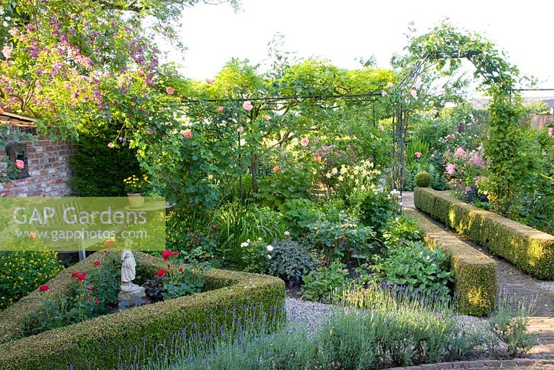 Mediterranean garden with triangular rose bed and stone statue, Lavandula planting in foreground and clipped Buxus hedging