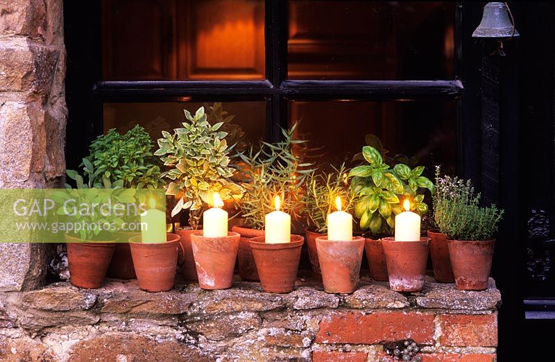 Candles in terracotta pots on windowsill with potted herbs - The Oast Houses, Hampshire 