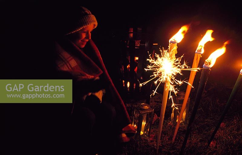 Child with sparkler in garden with metal fire basket and flares