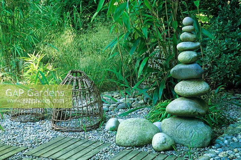 Sculptural tower of large pebbles with wooden panels inset in to a pebble path in a seaside style garden with grasses and bamboos - Designed by Alan Titchmarsh at Barleywood, Hampshire