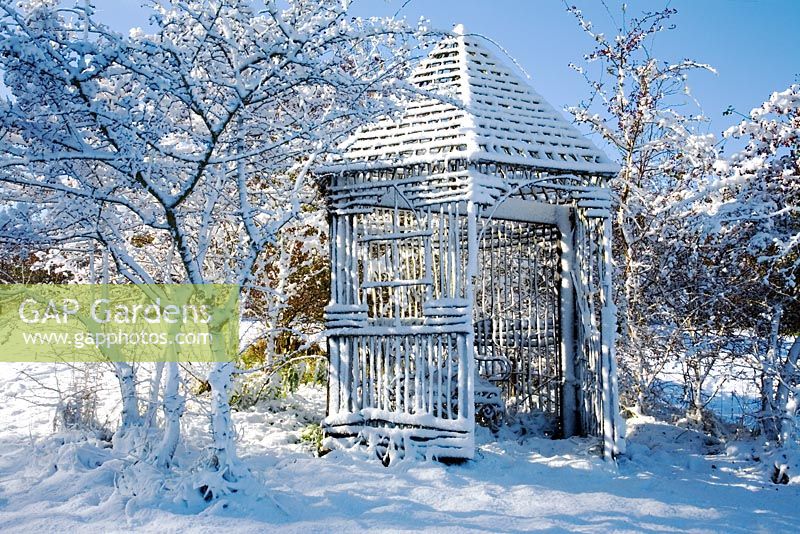 Fresh covering of snow on a rustic wooden gazebo in country garden with Fraxinus trees