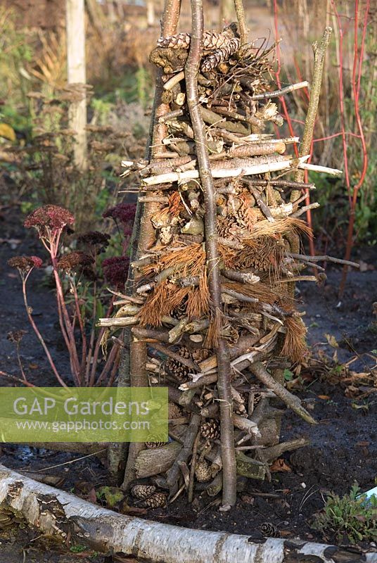 Wooden 'tripod' packed with twigs and fir cones to provide dark nooks and crannies in which insects such as ladybirds, lacewings and bees can overwinter in a wildlife garden - The Eco Garden, Trentham Gardens, Staffordshire 