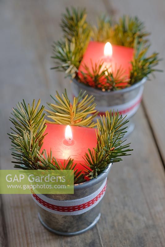 Red candles in mini zinc buckets with fir tree foliage and ribbon as a table decoration.