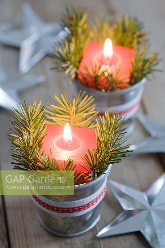 Red candles in mini zinc buckets with fir tree foliage and ribbon as a table decoration.