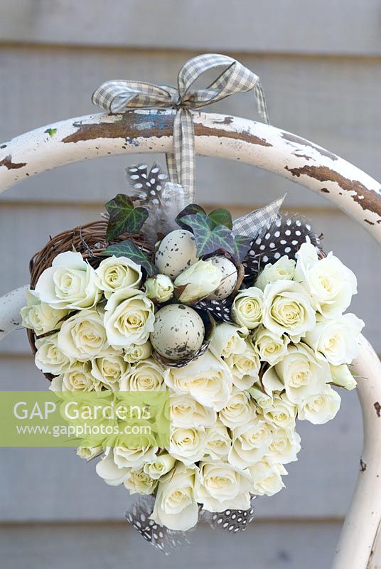White rose heart wreath with speckled eggs, tied to back of a rustic chair