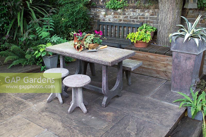 Conran table and stools on raised seating area in a small urban garden 