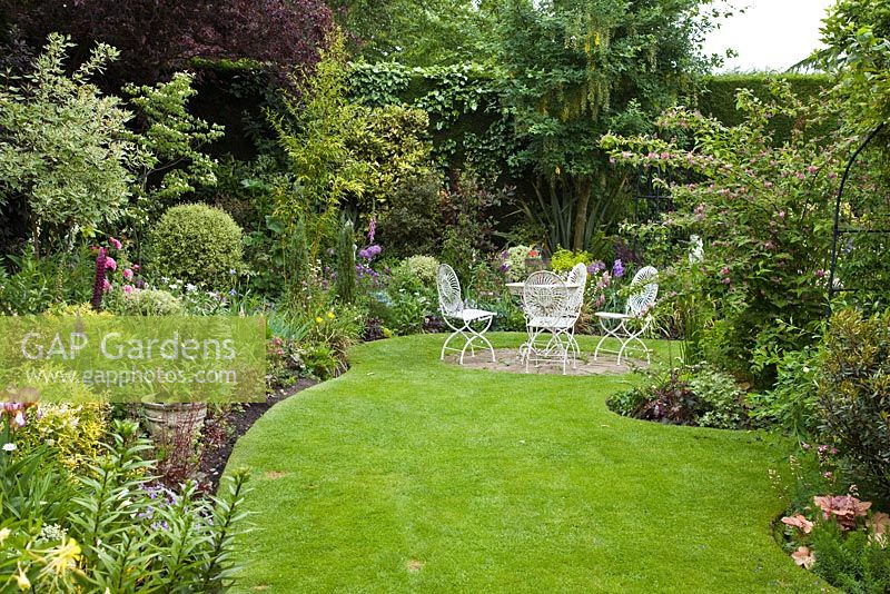 Mixed borders and seating area on lawn with ornate metal table and chairs in early summer - Dorset House NGS, Staffordshire 