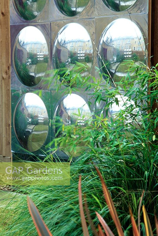 Detail of stainless steel wall sculpture with convex forms, planting includes Stipa, Phormium and bamboos