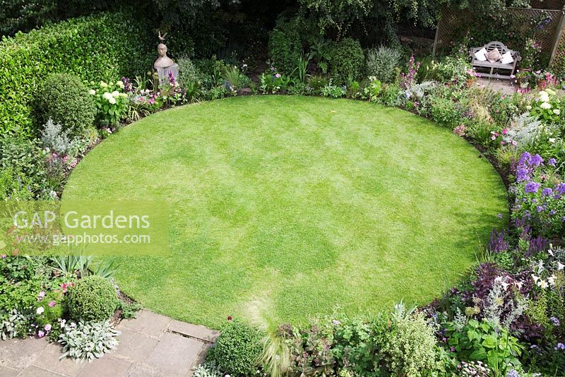 Overview of small Urban garden packed full of plants simply designed around a central circular lawn