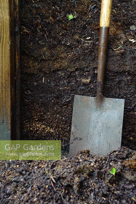Garden spade next to garden compost heap showing different layers of rotted plant material