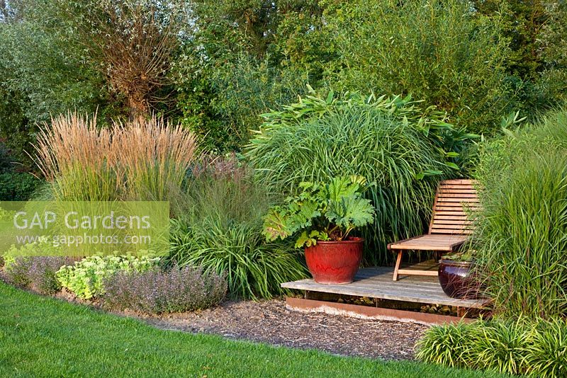 Decked seating area and border of Miscanthus, Molinia 'Transparent', Calamagrostis acutiflora, Sedum spectabile 'Brillant', Sedum 'Matrona', Calamintha, Nepeta 'Blue Cloud' and Liriope muscari