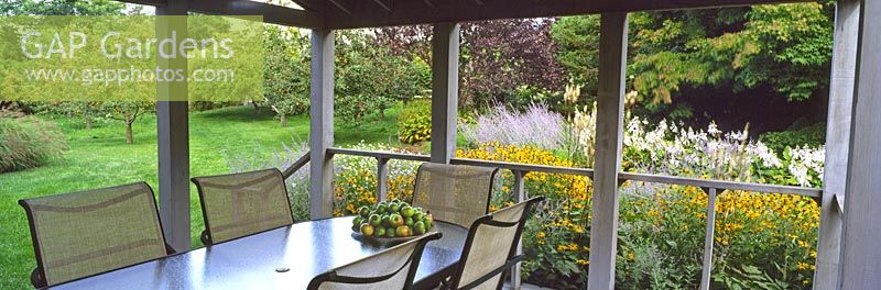 The verandah with view to orchard over large bed of flowering perennials including Rudbeckia fulgida 'Goldsturm', Perovskia atriplicifolia, Hosta sieboldiana and Cimicifuga - Rifkind Garden, Long Island, NY, USA