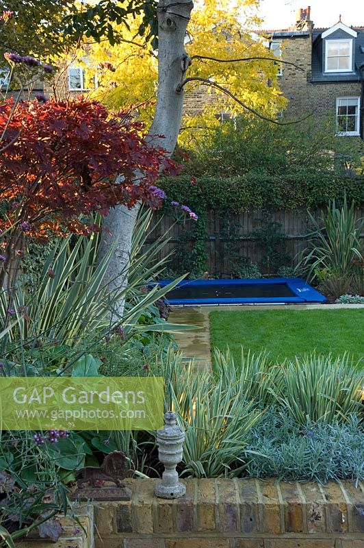 Contemporary urban garden with lighting, sunken trampoline and raised bed - London