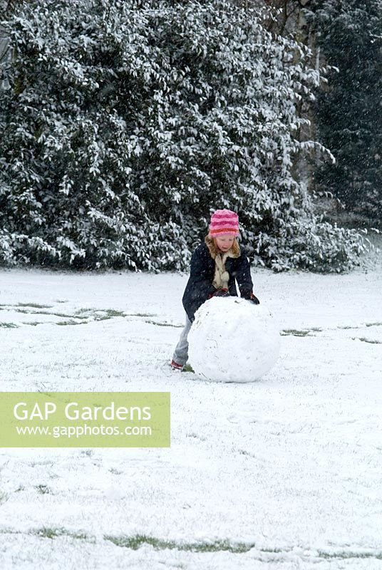 Child rolling a ball of snow to make a snowman in February