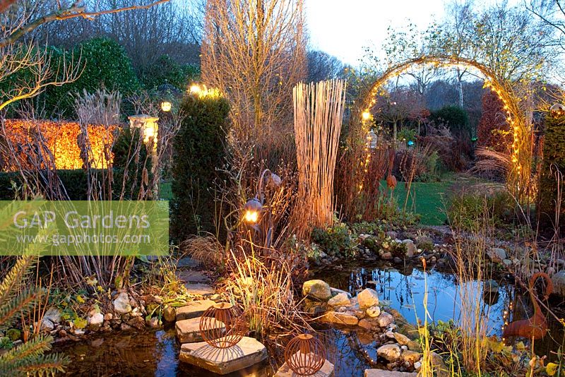 Winter garden with pond lit up at dusk

