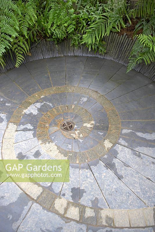 Slate and stone 'Ammonite' pattern flooring with central drainage surrounded by ferns