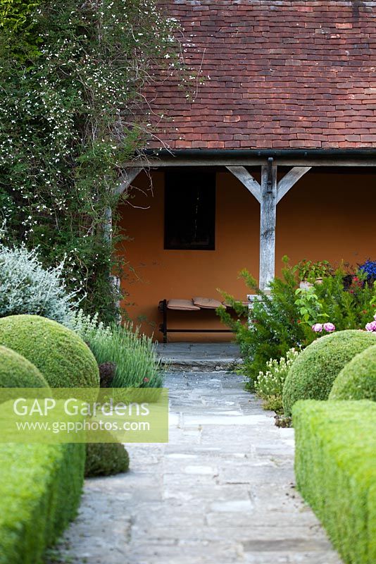 Stone pathway through formal topiary garden leading to verandah - Rymans, Sussex