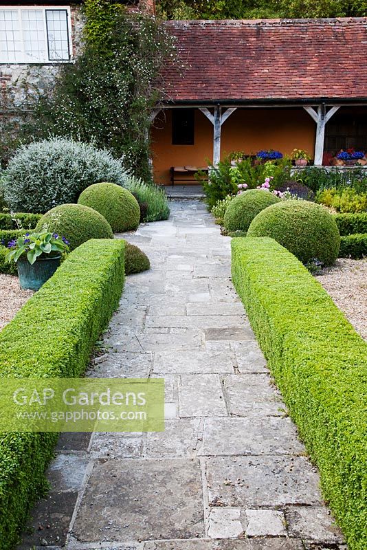 Stone pathway through formal topiary garden, leading to verandah - Rymans, Sussex